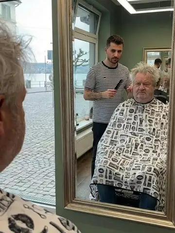 Friseur schneidet einem älteren Kunden die Haare, Blick durch die Glastür